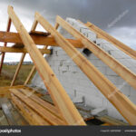 Unfinished house roofing construction with rain and rainy clouds on the sky. Wet roof beams.