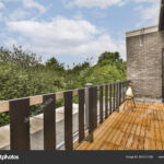 a wooden deck with trees in the background and blue sky above, taken from inside an open door to outside